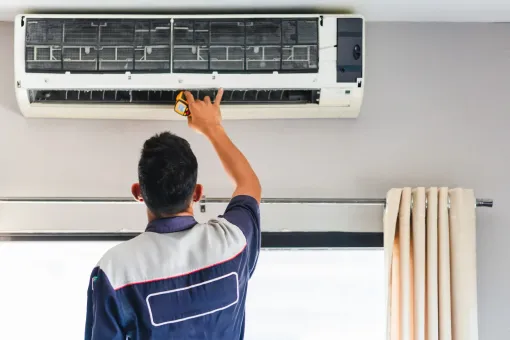 A technician repairing an air conditioning unit mounted on a wall indoors.