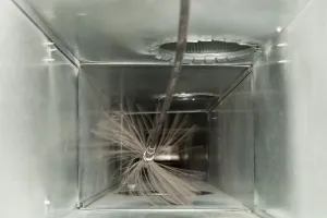 Brush cleaning a rectangular metal air duct.