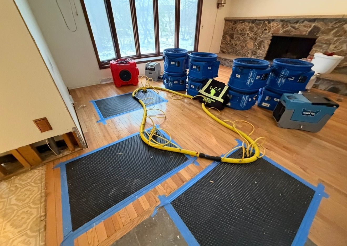 A room with water damage features floor-drying equipment, including suction mats taped to the wood floor and blue blowers.