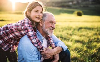 grandfather and granddaughter sit in green field
