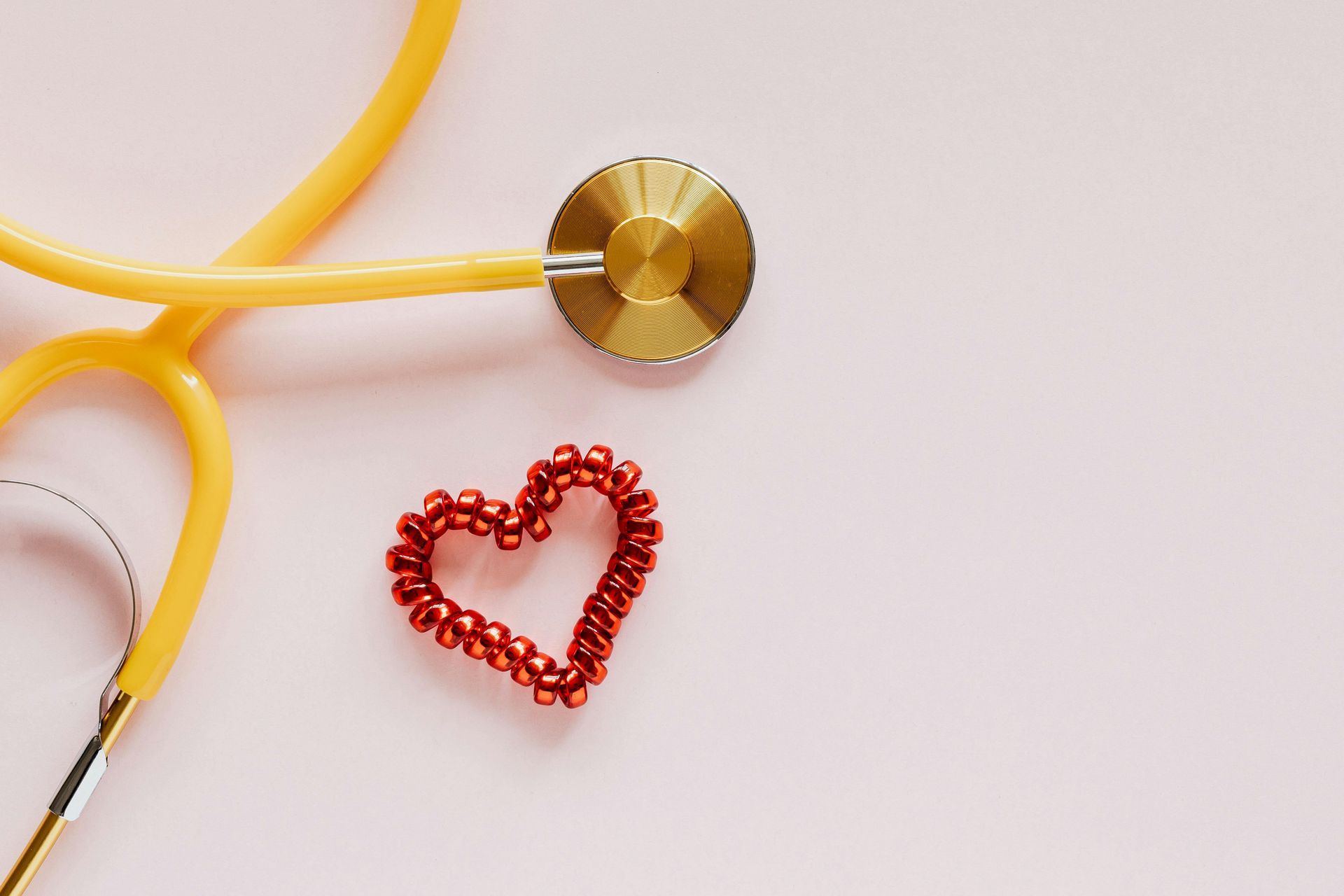 A stethoscope and a heart made of beads on a pink background.