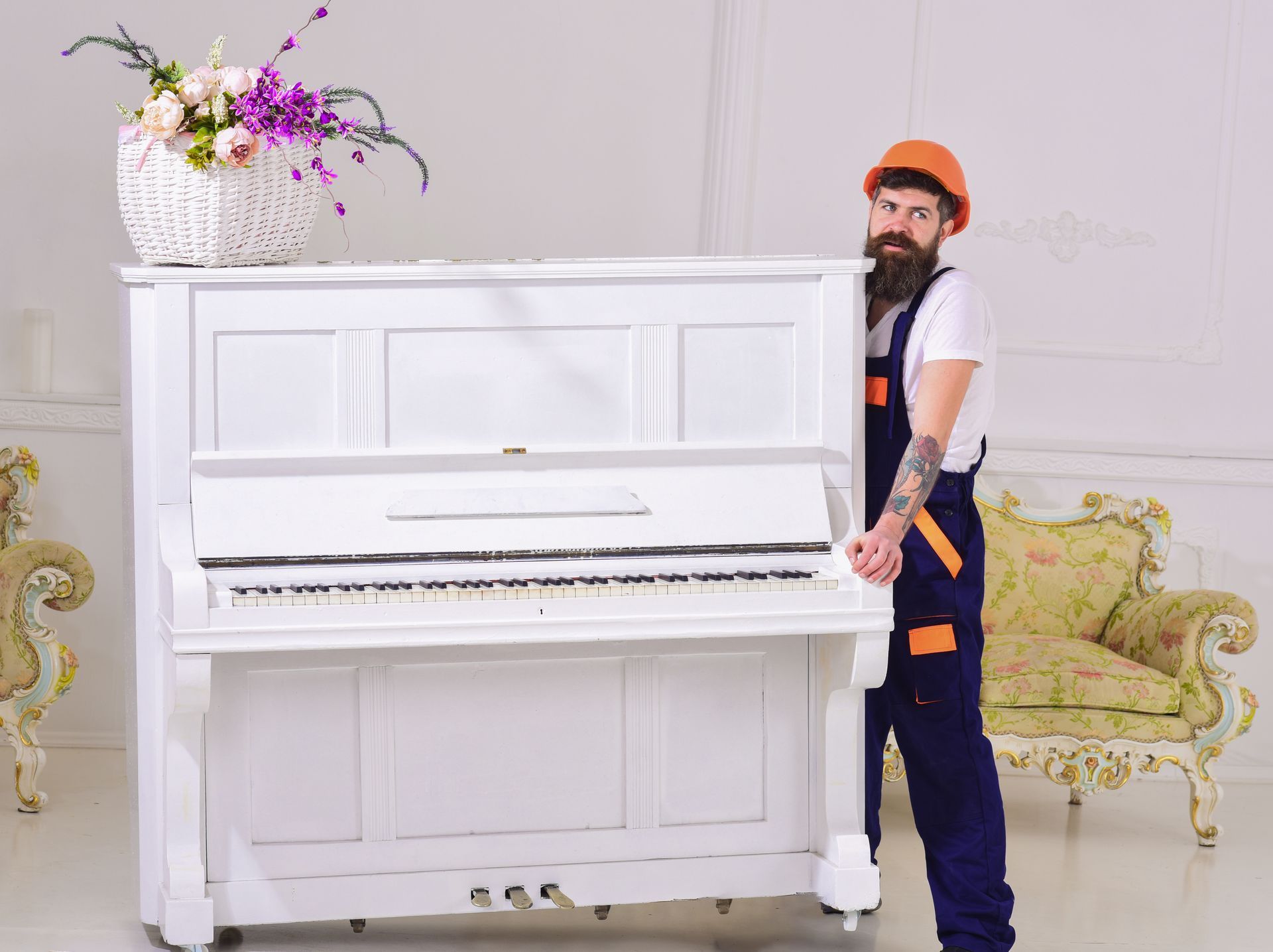 A man is carrying a white piano in a living room.