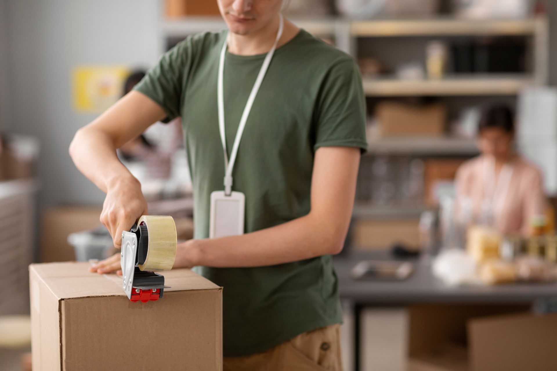 A man is taping a cardboard box in a warehouse.