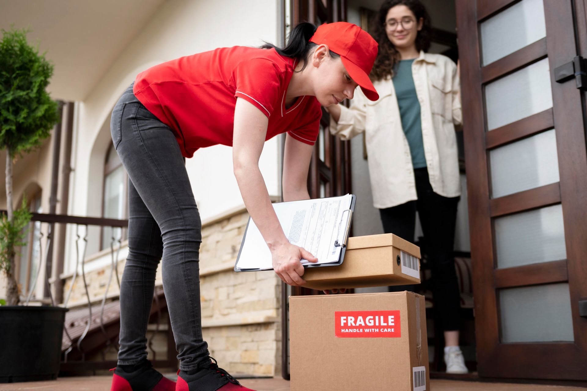 A woman is standing in front of a door holding a box and a clipboard.