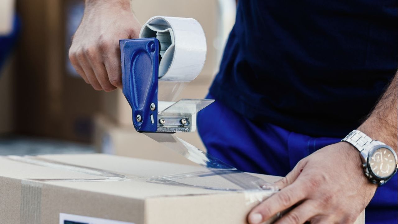 A man is taping a box with a blue tape dispenser