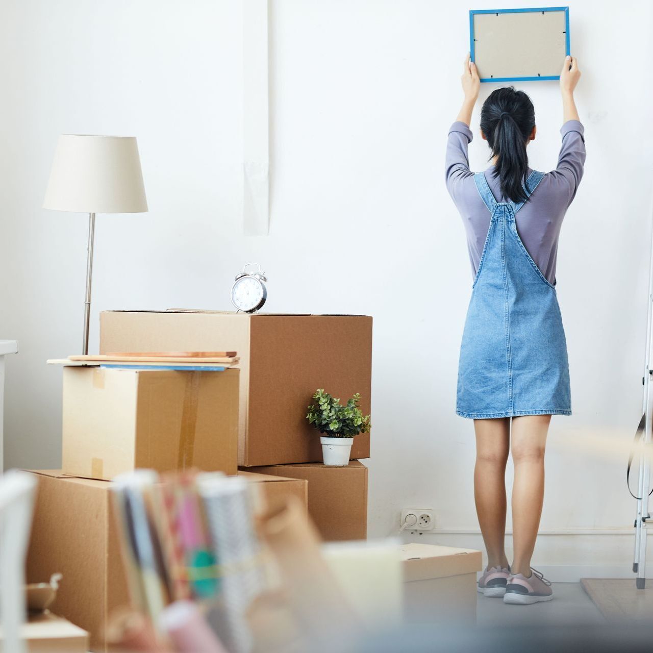 A woman in a blue dress is standing in a living room holding a picture frame.