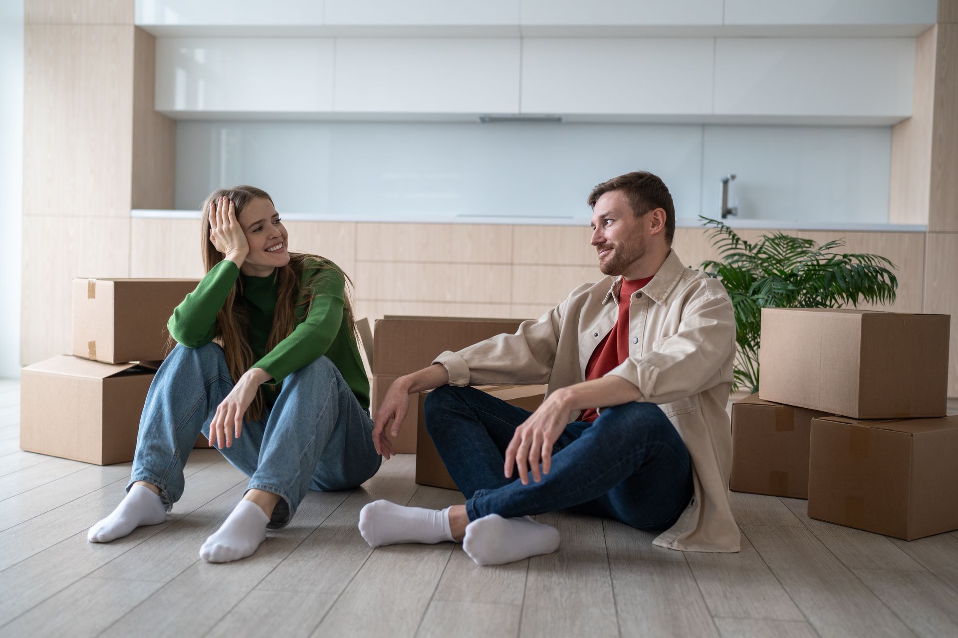 A man and a woman are sitting on the floor in their new home surrounded by cardboard boxes.