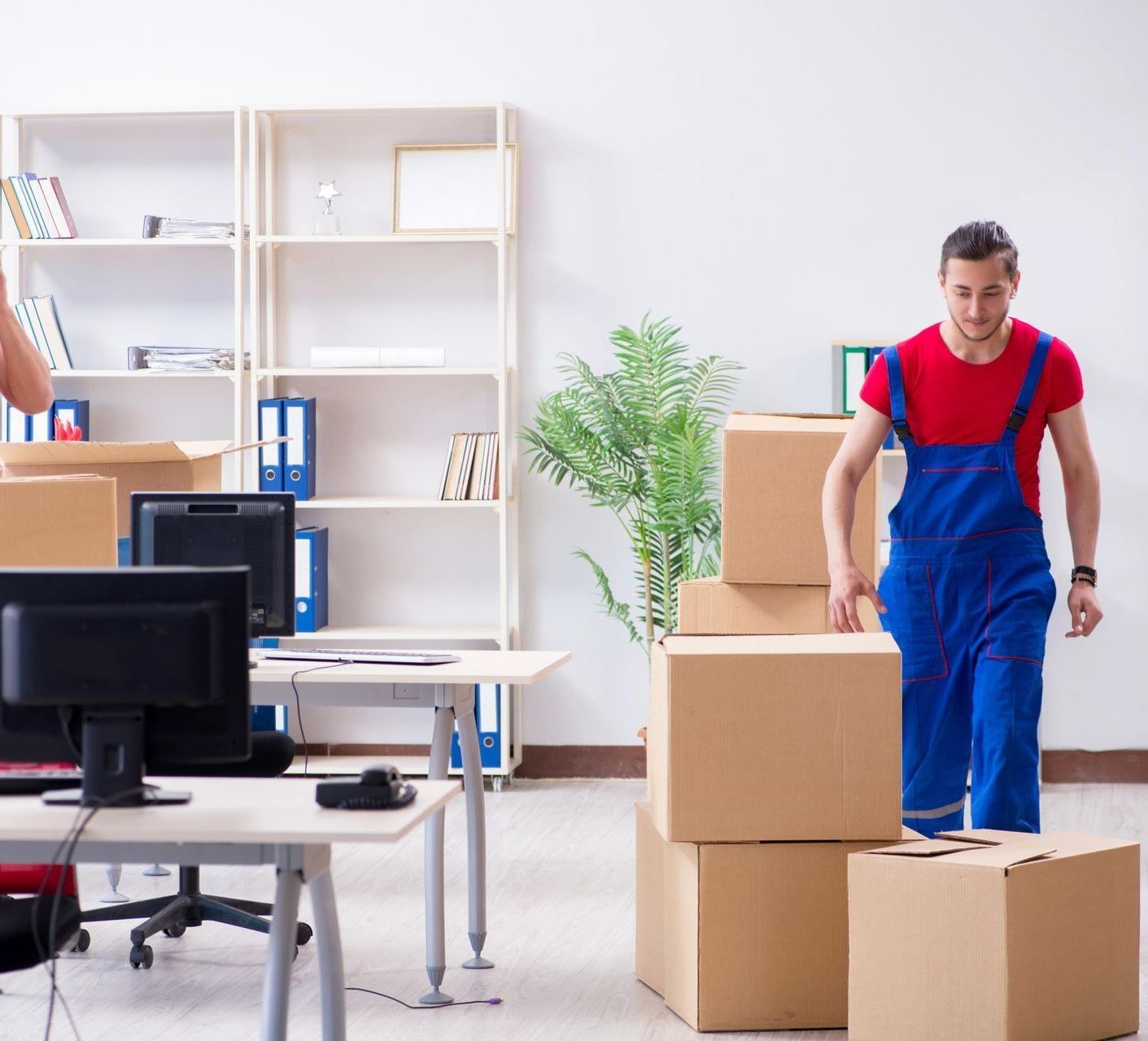 Two men are moving boxes in an office.