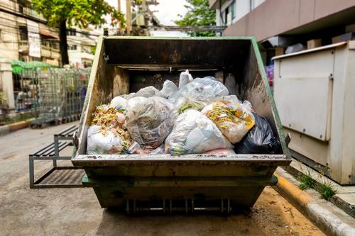 A dumpster filled with trash is parked on the side of the road.