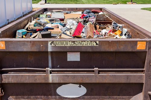 A dumpster filled with lots of trash is sitting on the side of the road.