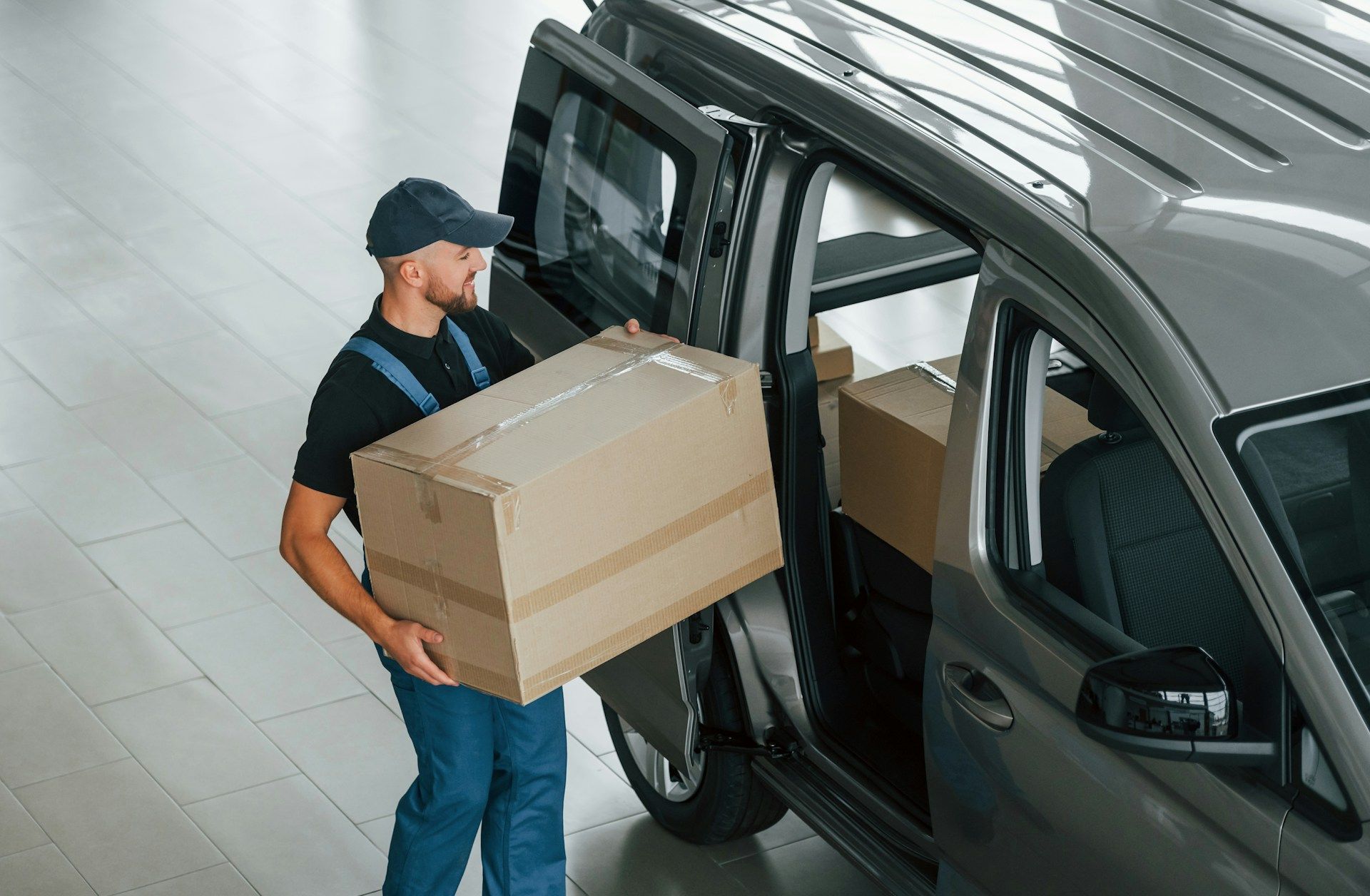 Delivery person loading boxes into a gray van. Indoors, person in uniform, carrying a large cardboard box.