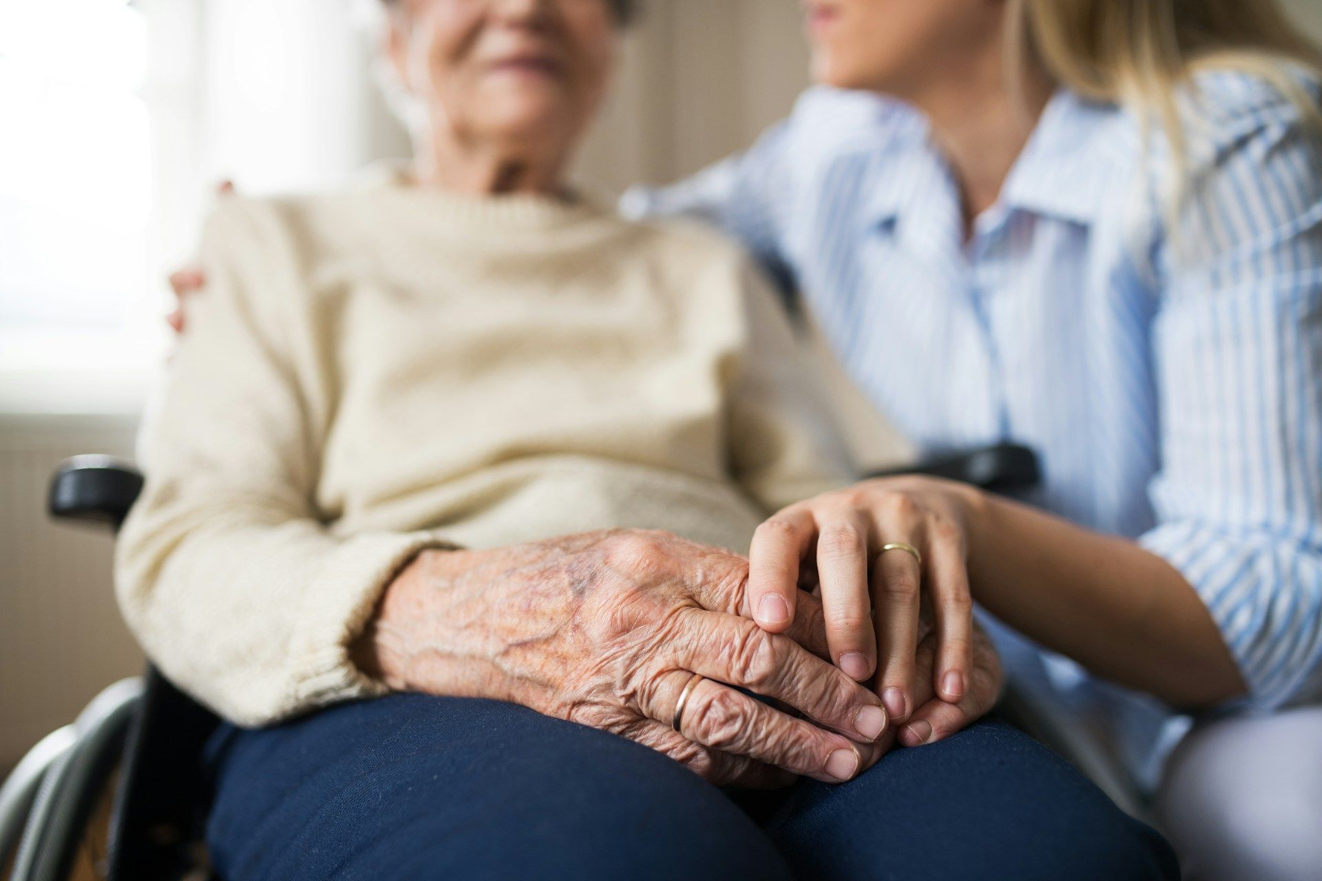 Elderly woman in a wheelchair with a caregiver holding her hand and arm.