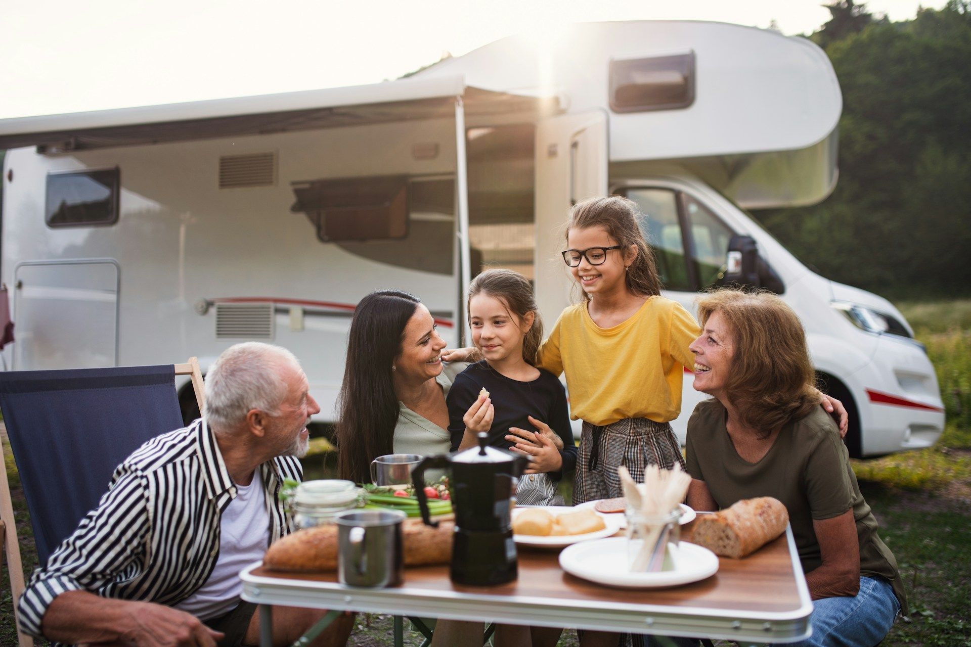 Family, including grandparents and children, eating outdoors by an RV.
