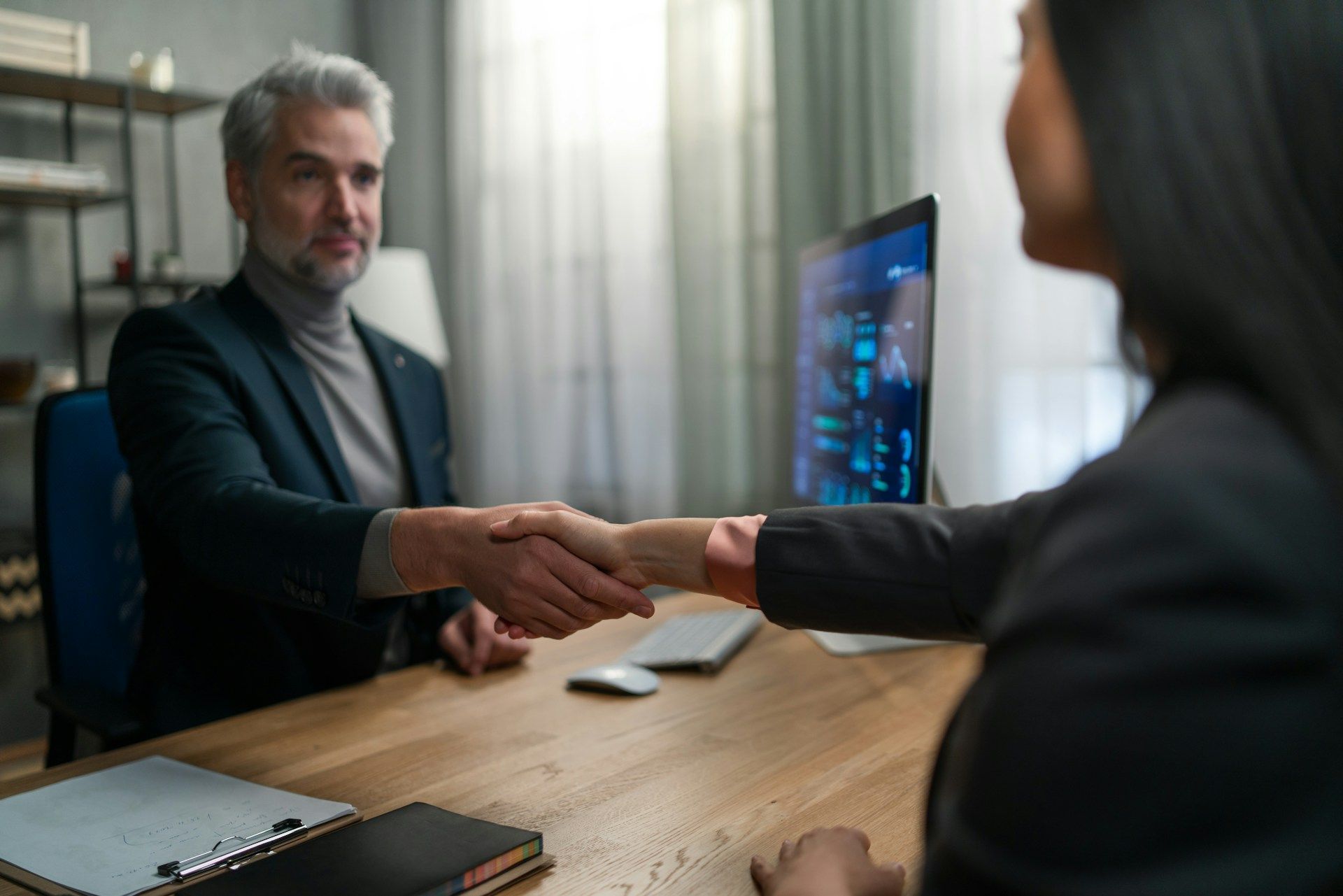 Man in suit shakes hands with woman at a desk in an office setting.