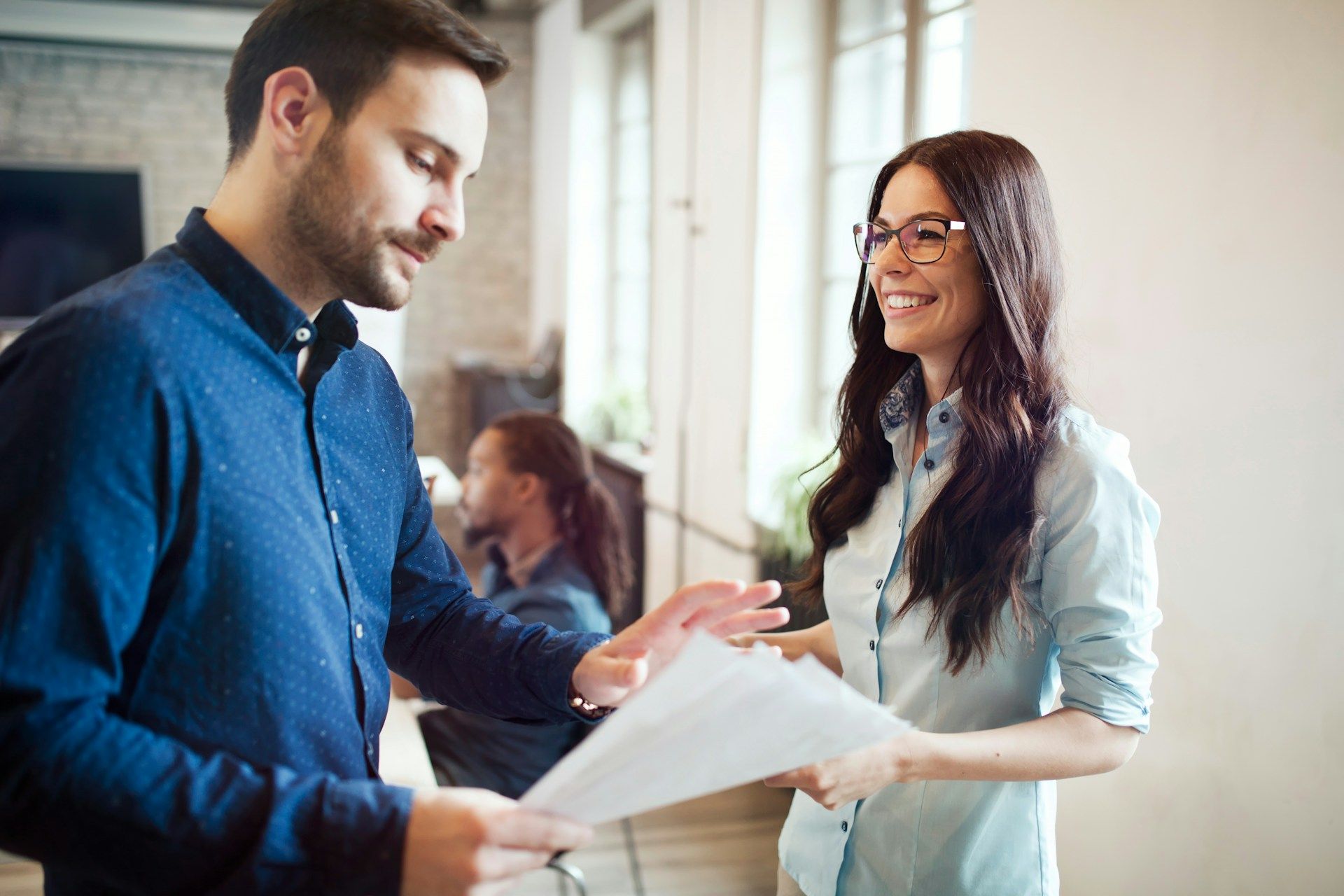 Man and woman smiling, reviewing papers together in a bright office setting.