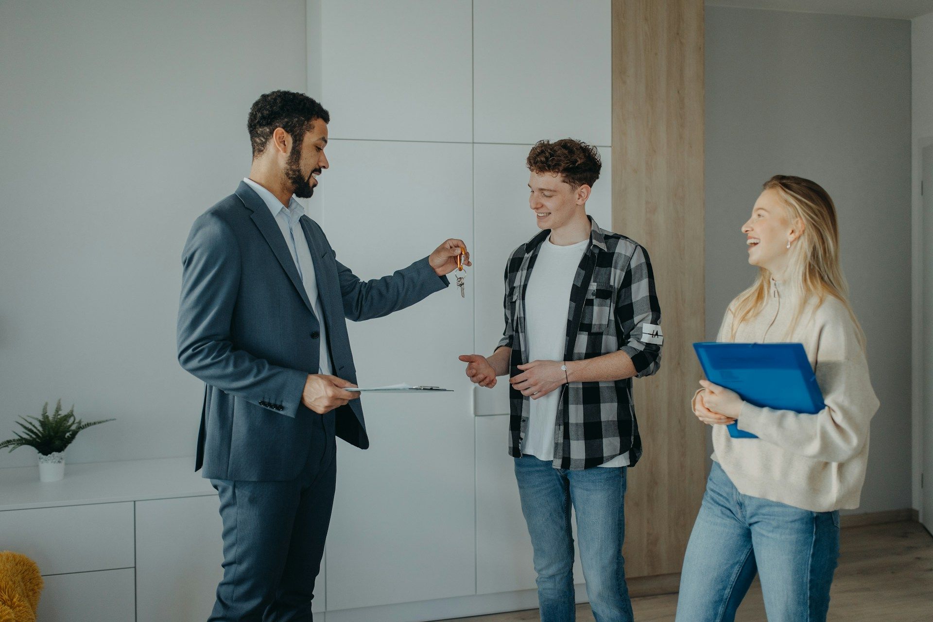 Real estate agent handing keys to a young couple in a bright apartment.