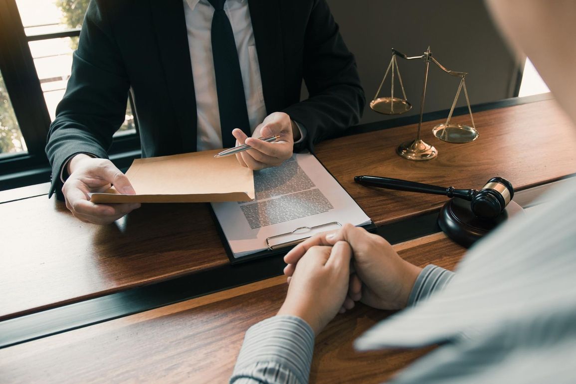 Lawyer hands client a document at a desk with scales of justice and gavel.