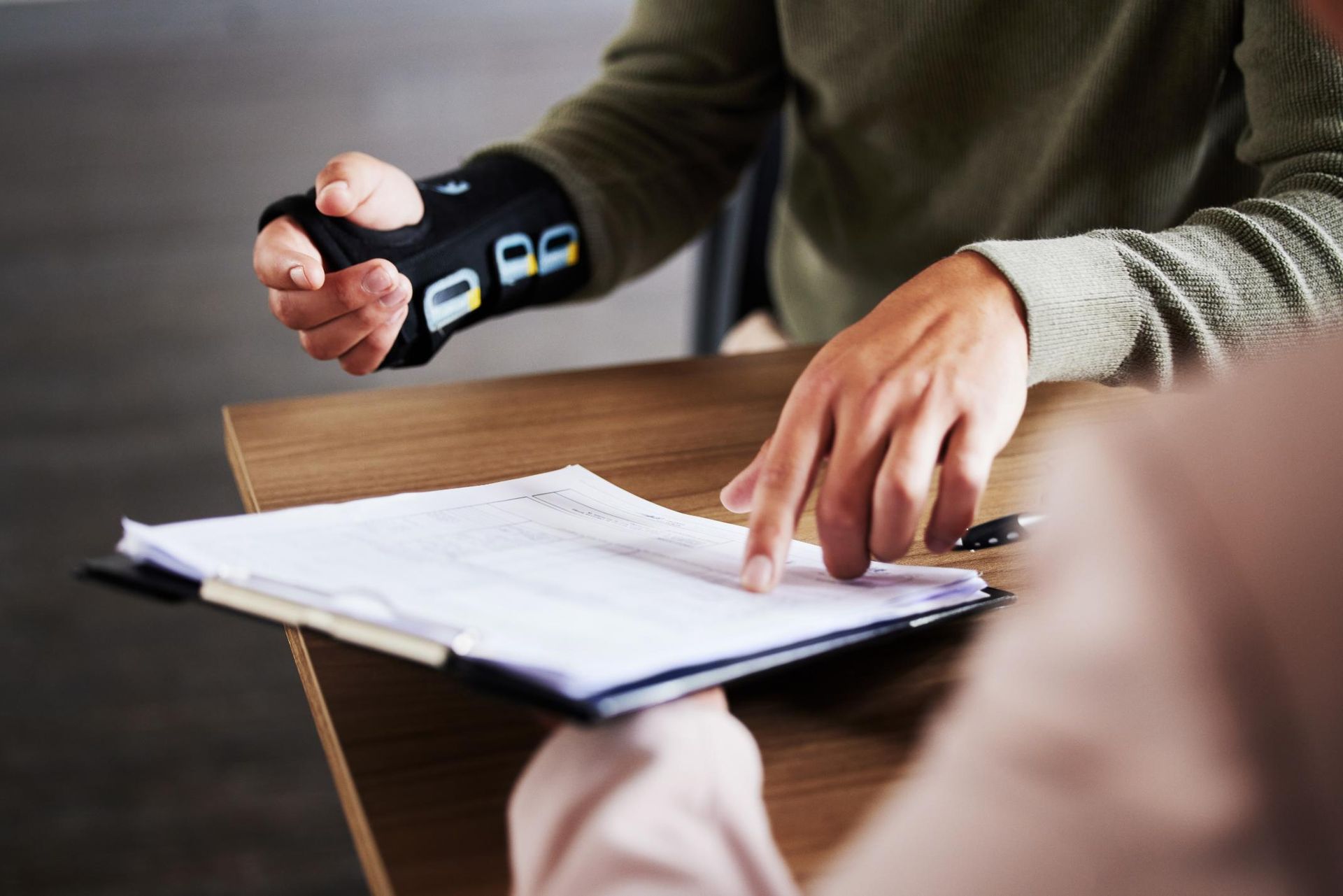 Person wearing a black wrist device interacting with another person over a document at a table.
