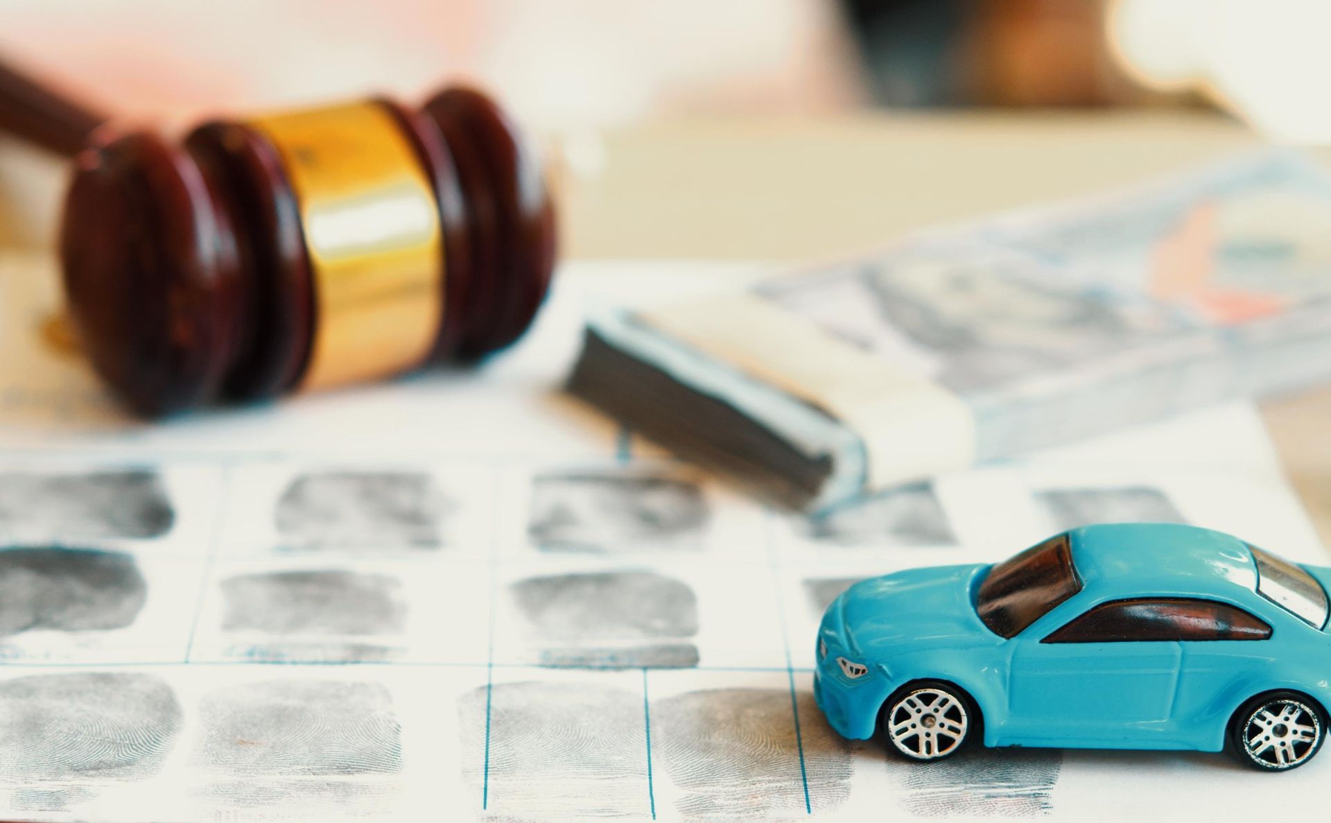 Miniature blue car, gavel, money, and fingerprints on a document.