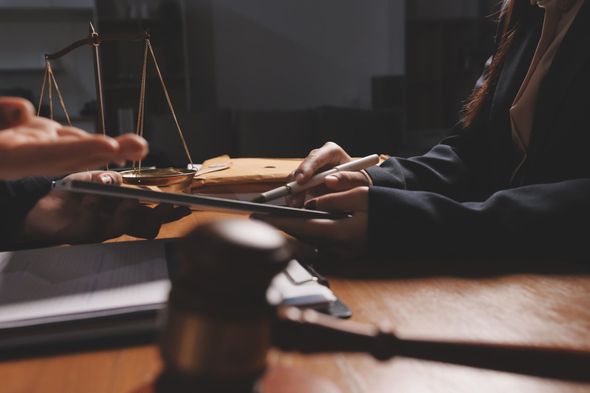 Woman in a blazer reviews documents with another person in a law office.