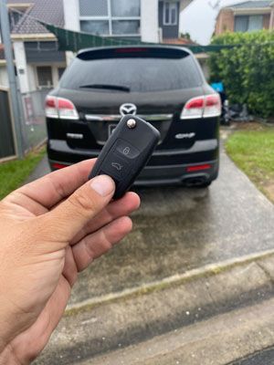A person is holding a remote control in front of a car.