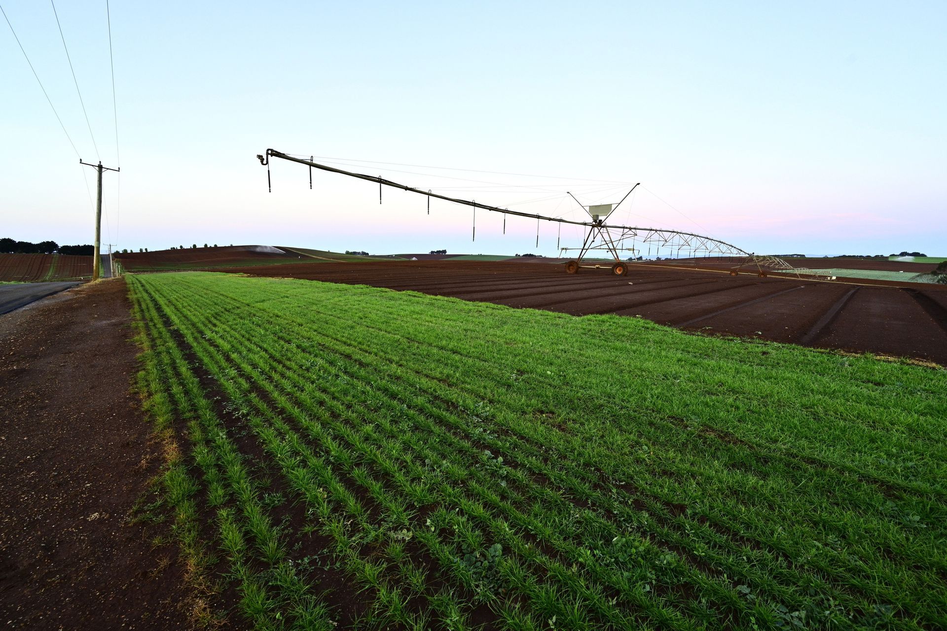 Woman in scrubs pointing at laptop, another woman in background. Desk with printer, keyboard, monitor.