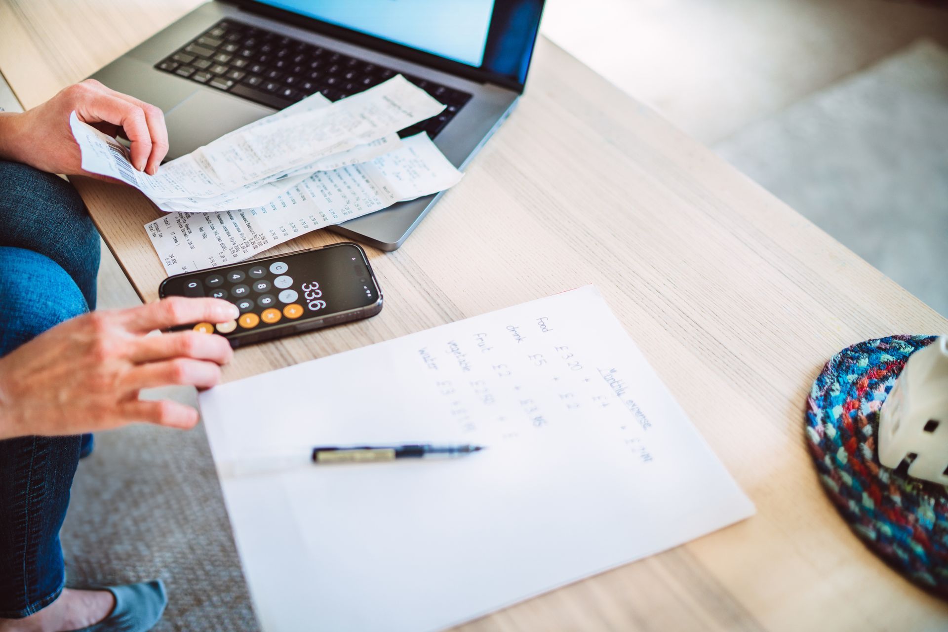 Person calculating finances with laptop, calculator, receipts, and notepad on a table.