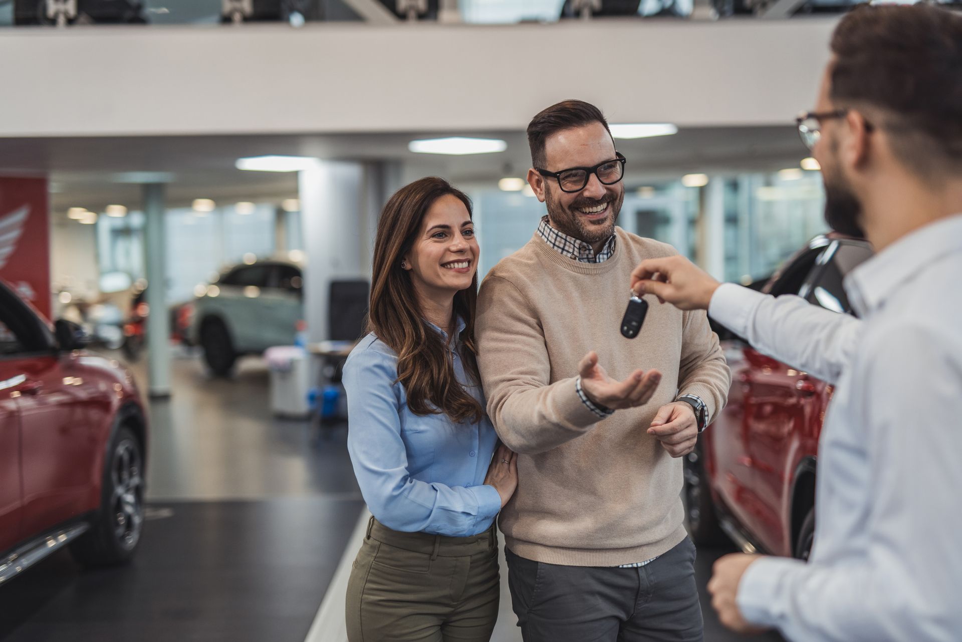 Couple receiving car keys from a salesperson in a car showroom, smiling.
