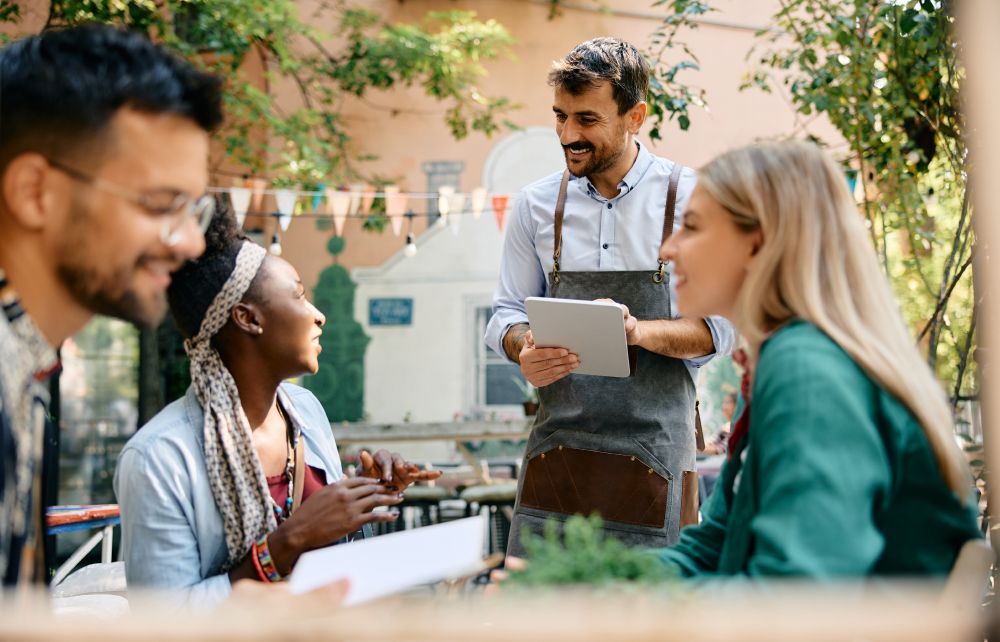 A group of people are sitting at a table in a restaurant talking to a waiter.