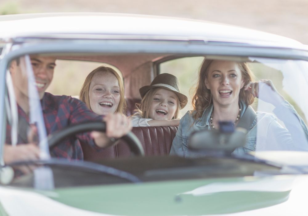 A family is sitting in a car and smiling.
