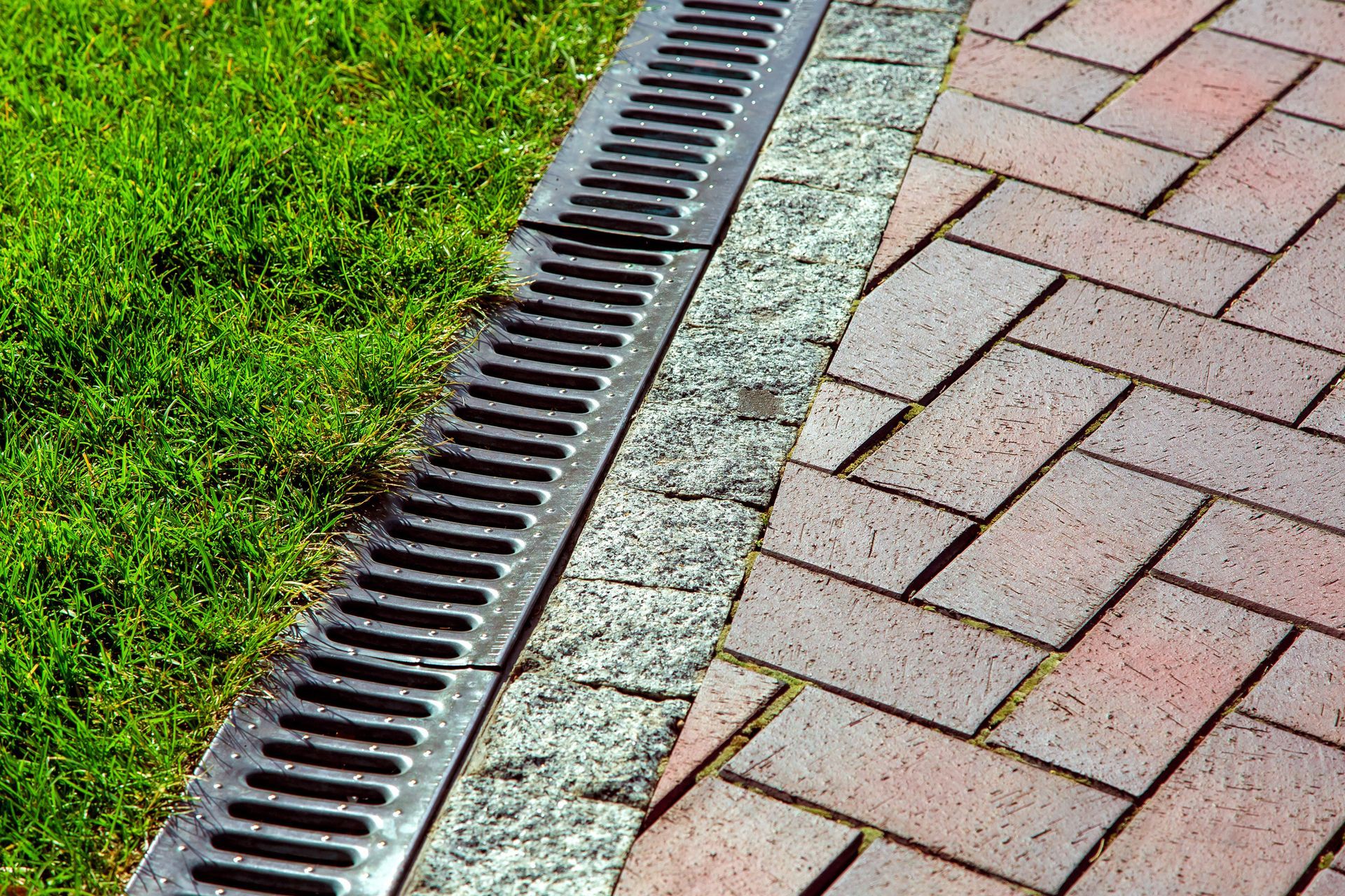A drain on the side of a brick walkway next to a grassy area.