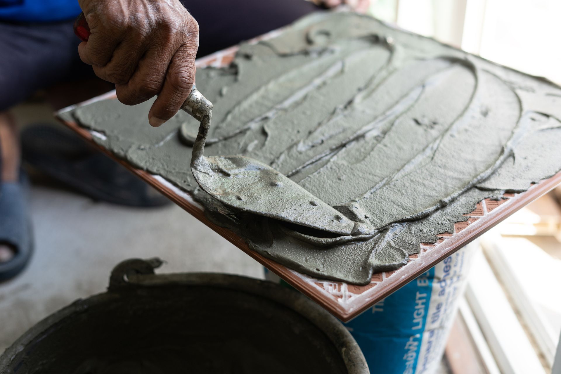A person is spreading cement on a tile with a trowel.
