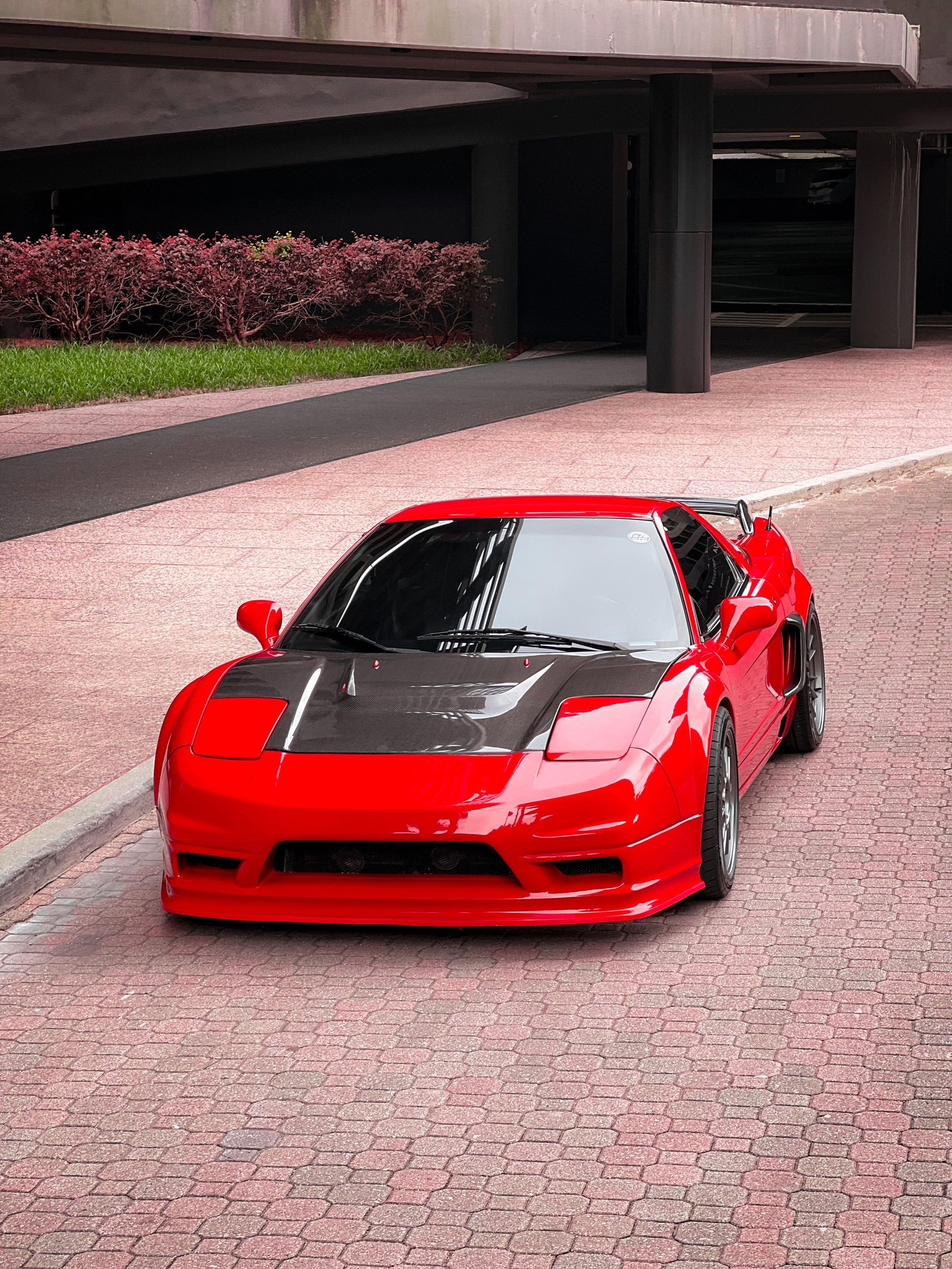 A vibrant red Acura NSX with a glossy carbon-fiber hood, parked stylishly on a brick-paved street.