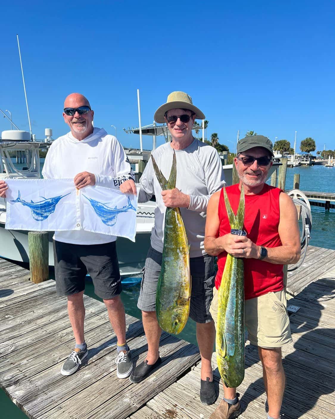 Three men are standing on a dock holding fish.
