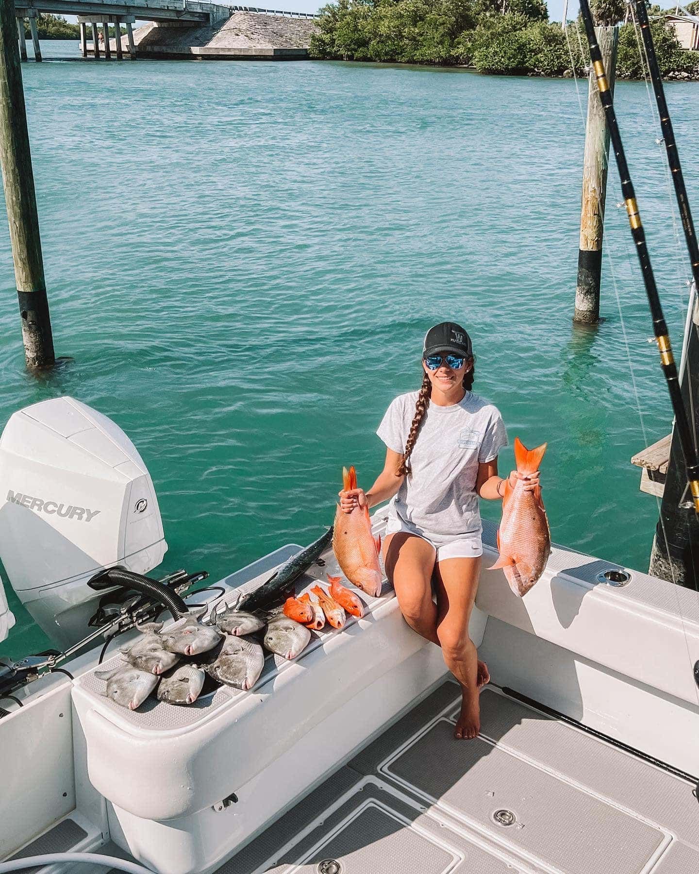 A woman is sitting on the back of a boat holding two fish.