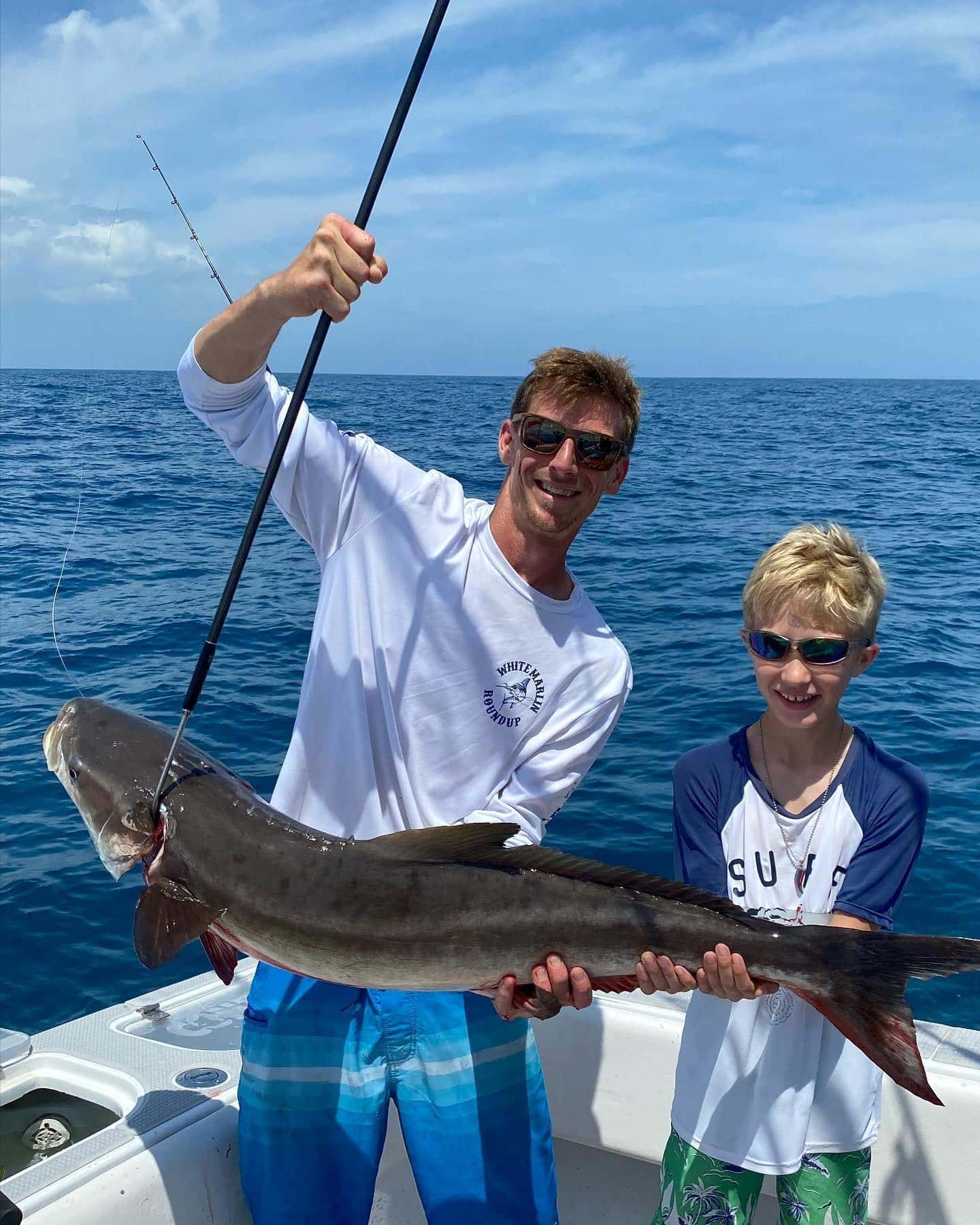 A man and a boy are holding a large fish on a boat.