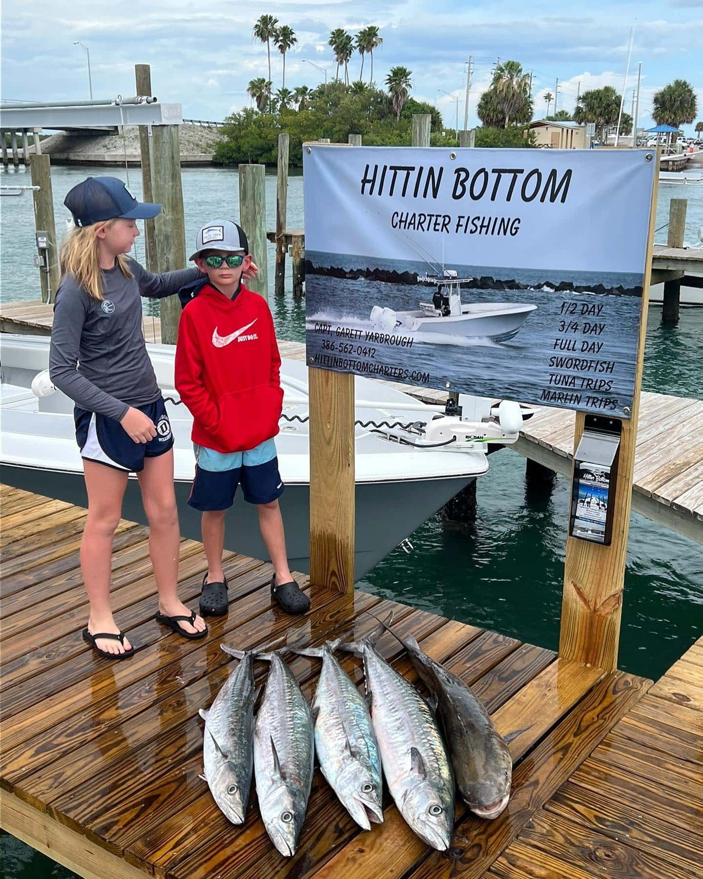 A boy and a girl are standing on a dock next to a bunch of fish.