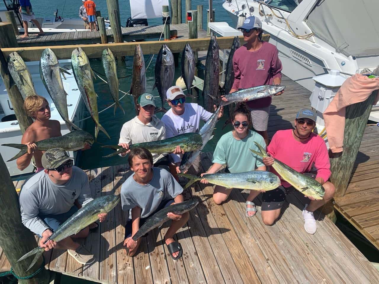 A group of people are standing on a dock holding fish.