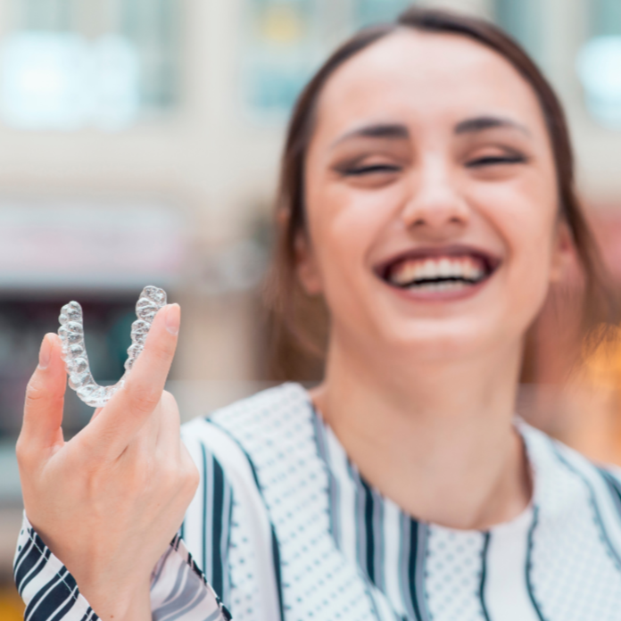 Woman smiling, holding clear aligner for teeth straightening.