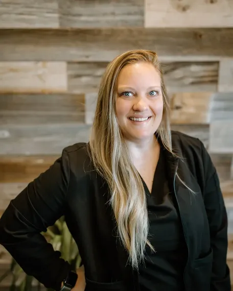 a woman in a black jacket is smiling in front of a wooden wall