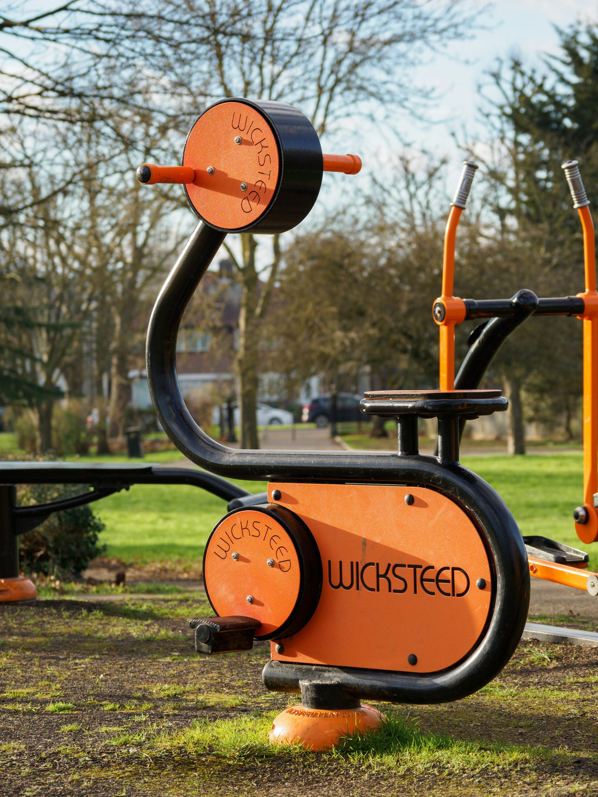 Orange-and-black outdoor exercise machine in a park, with curved metal frame and seating