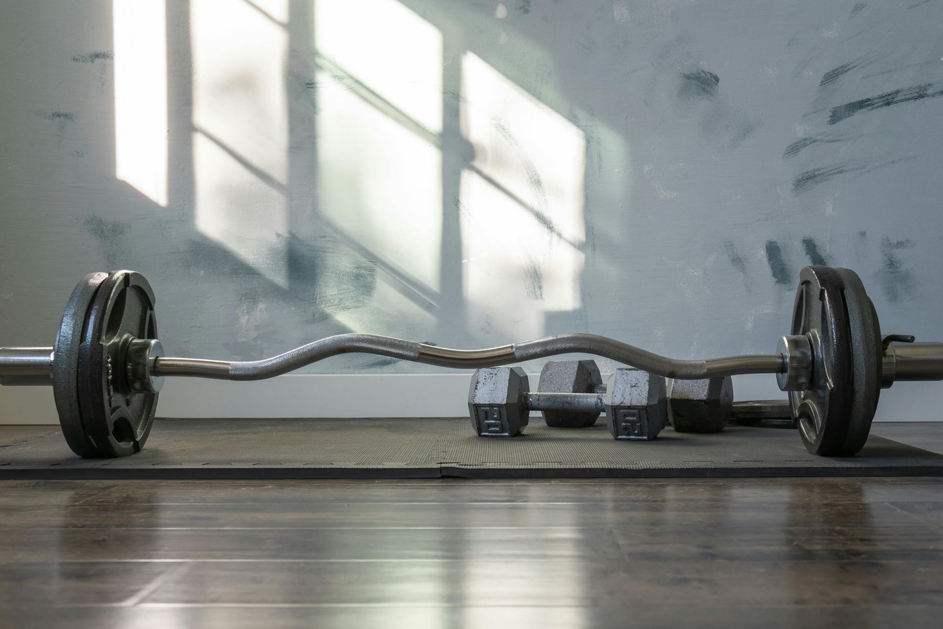 Barbell with weight plates on a gym floor in a bright, minimalist room