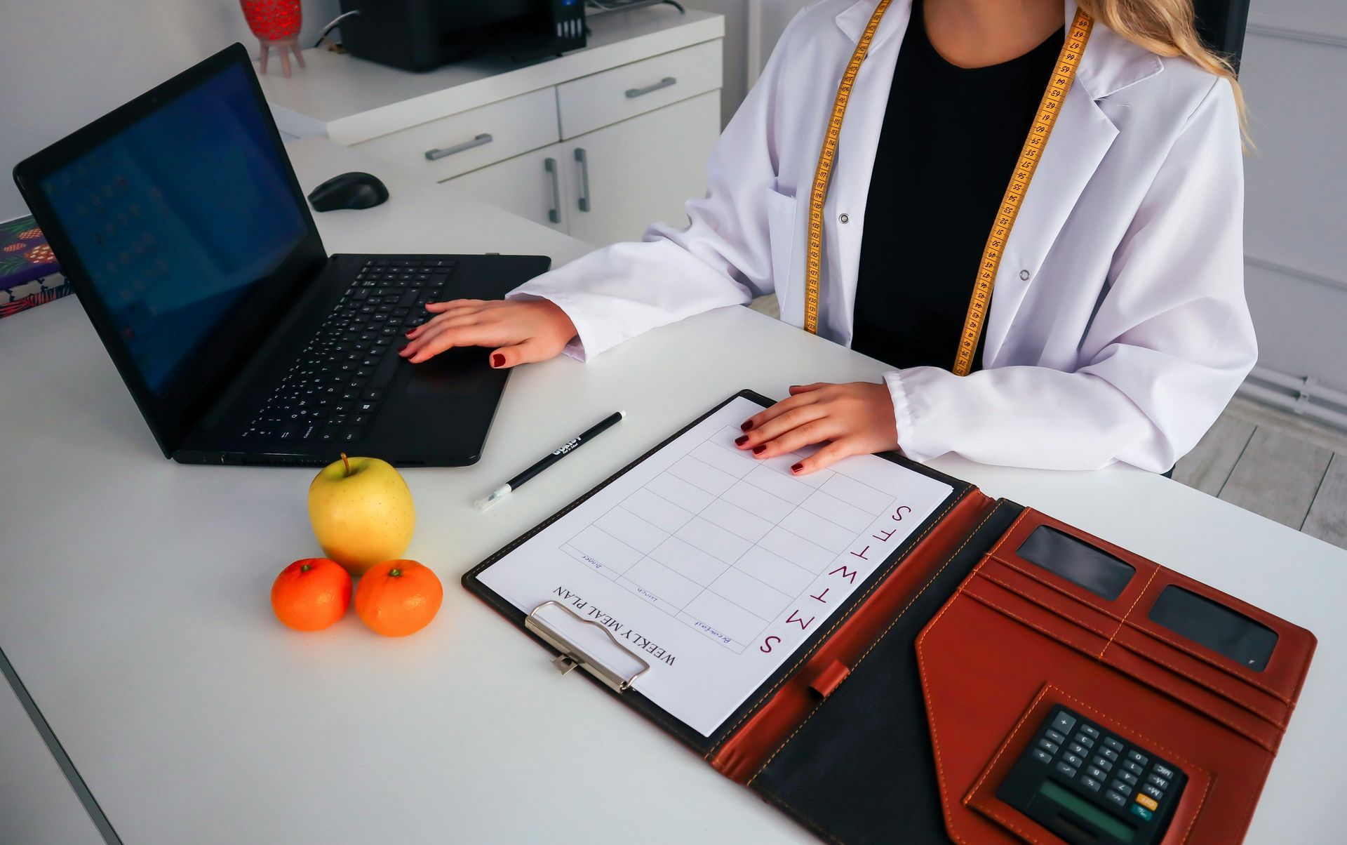 Person at a desk with laptop, notebook, calculator, and oranges in an office setting