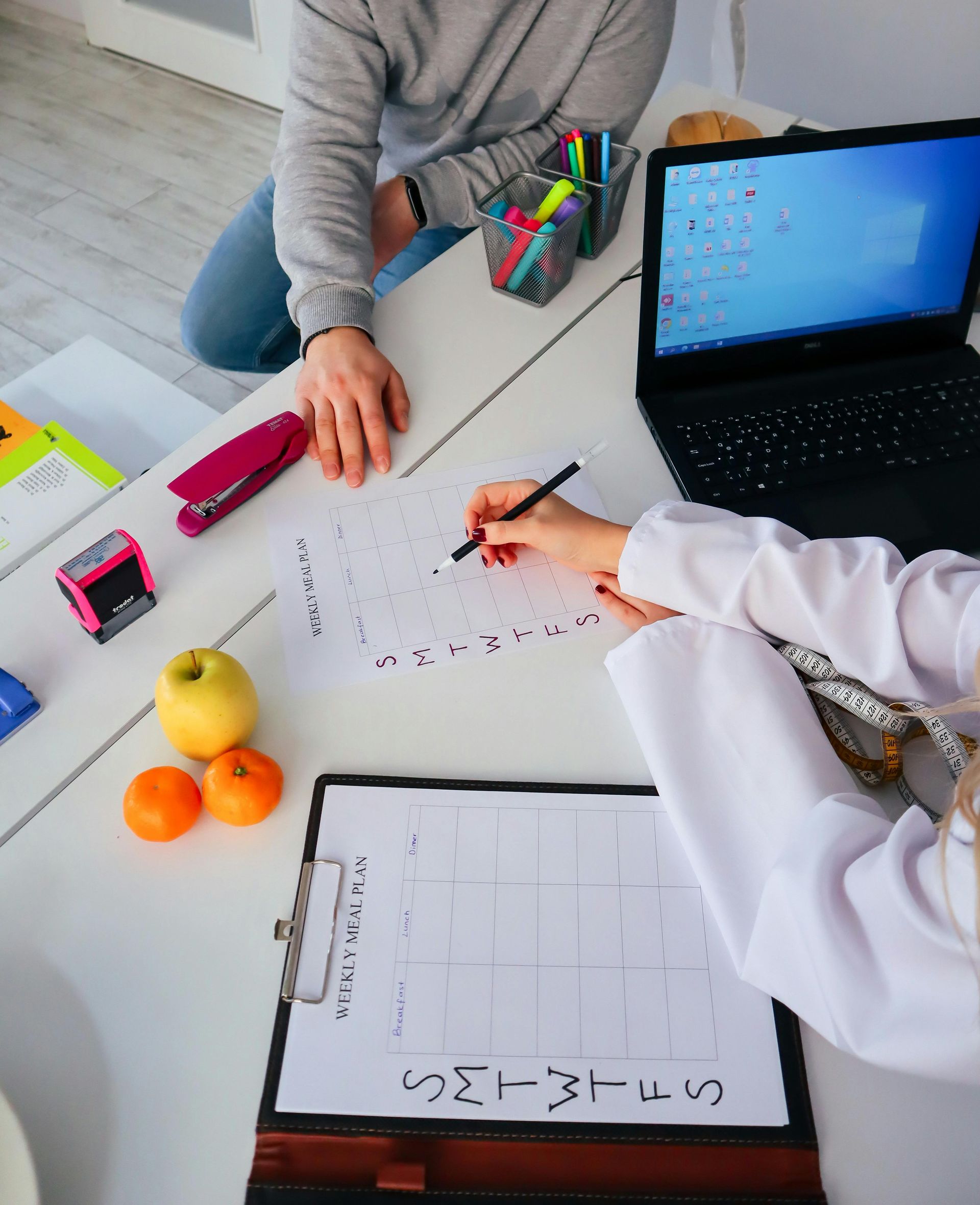 People doing a worksheet at a table with a laptop, clipboard, and fruit nearby