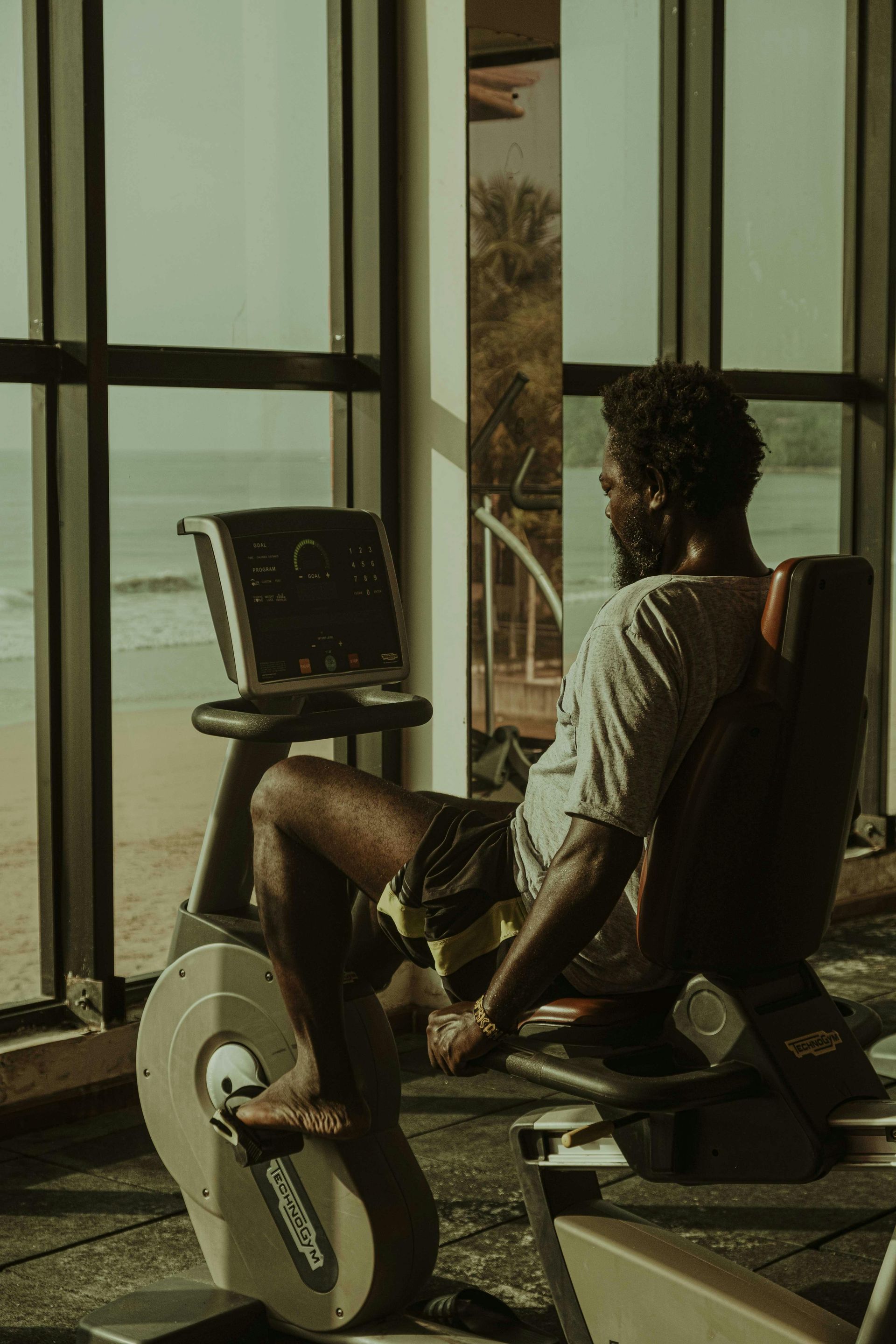 Person on an exercise bike in a bright room with large windows, facing a monitor