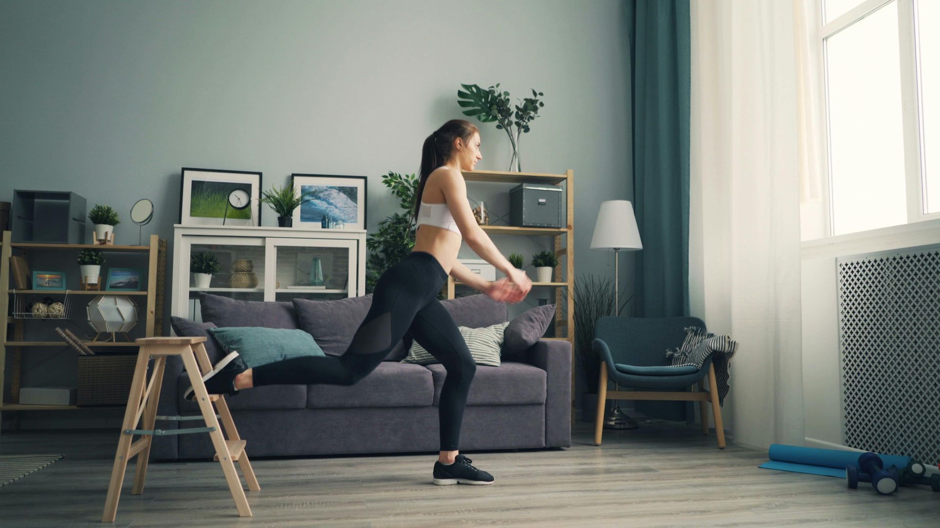 Person exercising in a living room, doing a standing leg stretch beside a couch.