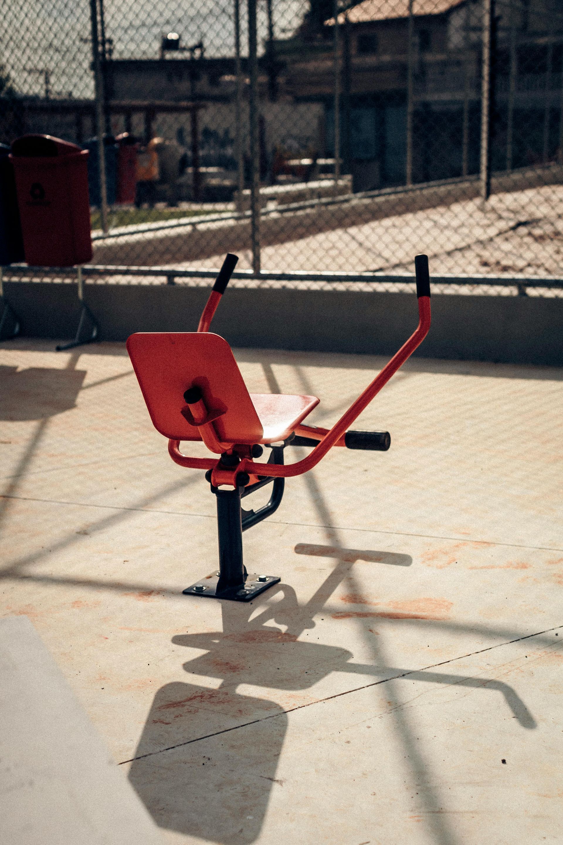 Red outdoor exercise machine on a concrete court in front of a chain-link fence.