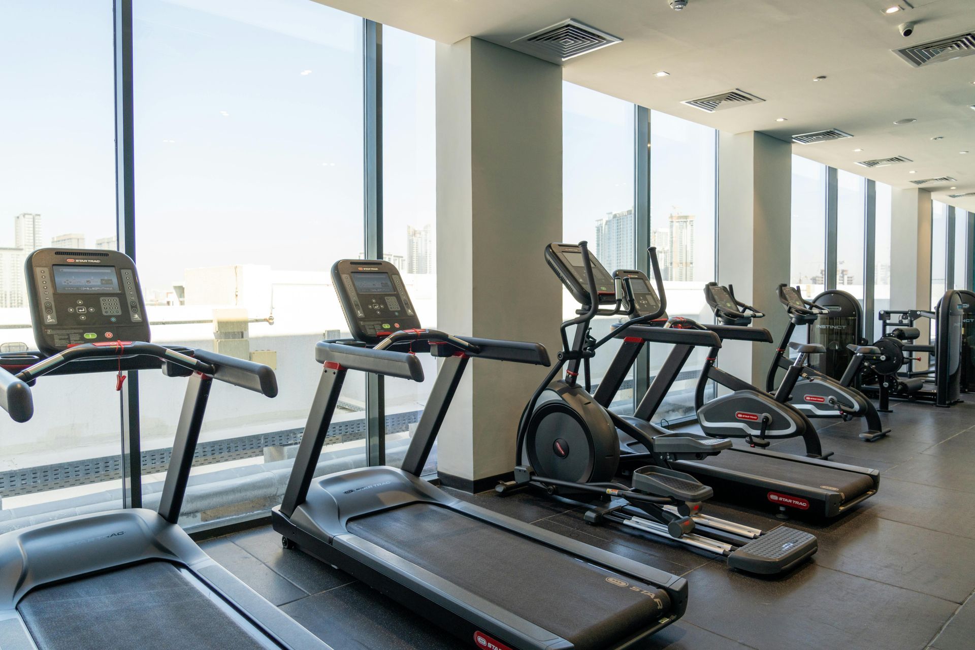 Modern gym with treadmills and elliptical machines beside large windows