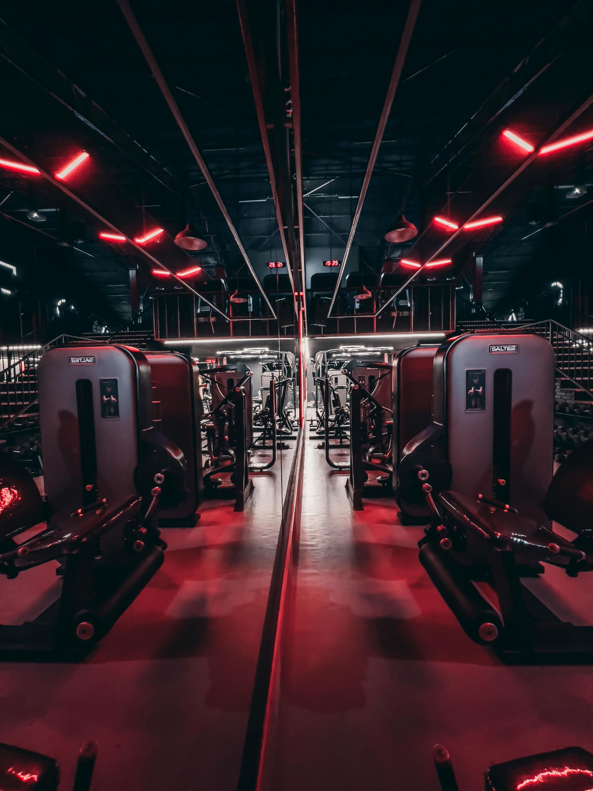 Red-lit gym with rows of workout machines and mirrored walls