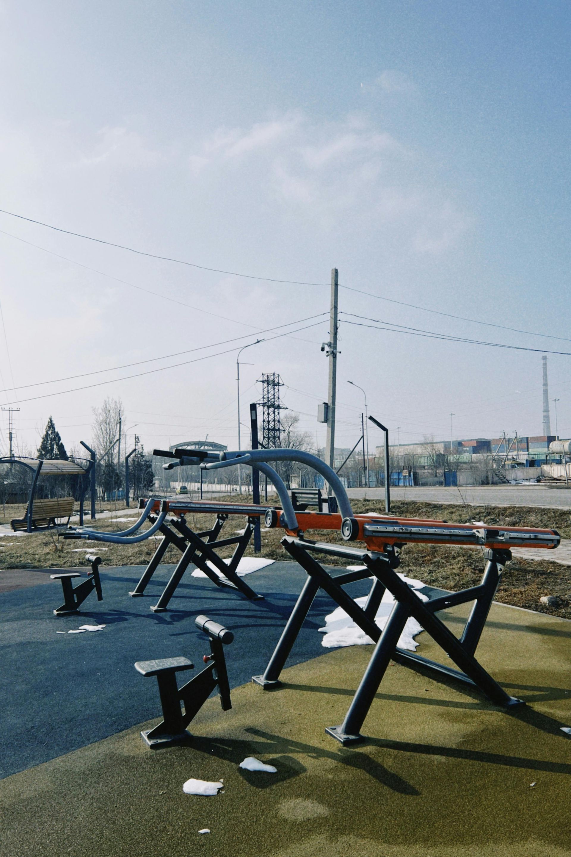 Outdoor fitness park with metal exercise equipment on a grassy field under a bright sky